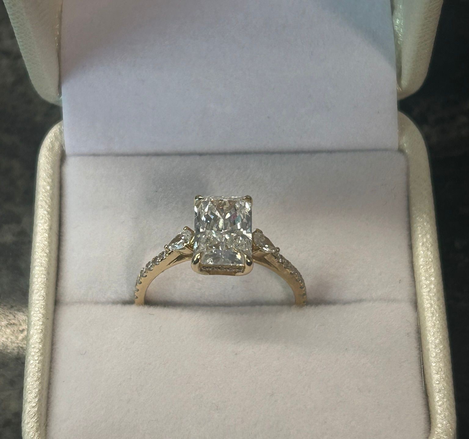 Gold engagement ring with a rectangular diamond centerpiece in a white box.